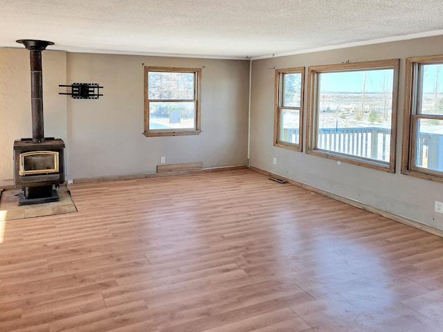 unfurnished living room featuring a textured ceiling, wood finished floors, visible vents, baseboards, and a wood stove