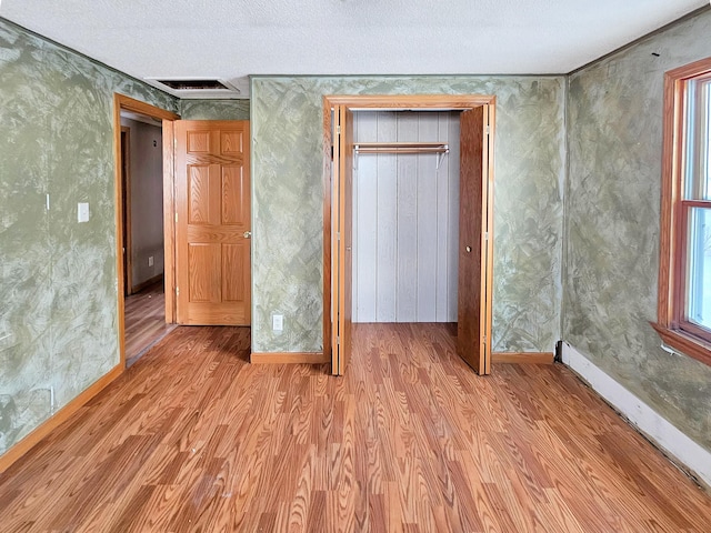 unfurnished bedroom featuring wood finished floors, visible vents, baseboard heating, and wallpapered walls