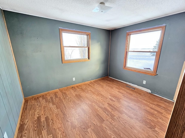 spare room featuring baseboards, a textured ceiling, visible vents, and wood finished floors