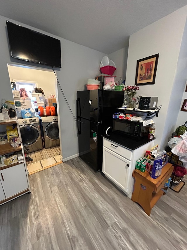 kitchen with dark countertops, washing machine and clothes dryer, light wood-type flooring, black appliances, and white cabinetry