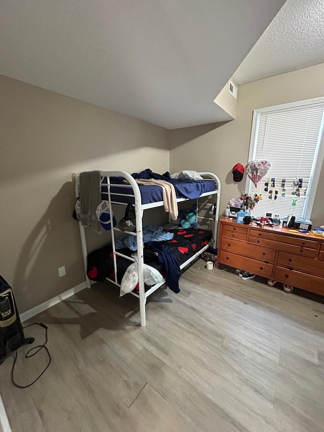 bedroom with a textured ceiling, wood finished floors, visible vents, and baseboards