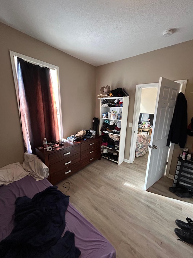 bedroom with baseboards, light wood-style flooring, and a textured ceiling