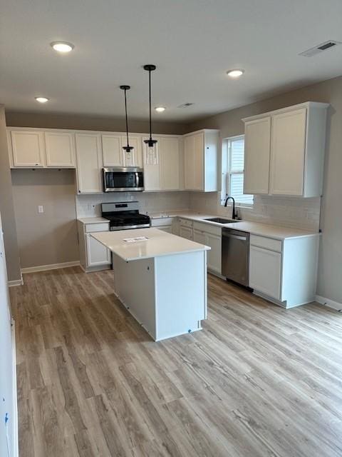 kitchen with a center island, appliances with stainless steel finishes, light wood-style floors, white cabinetry, and a sink