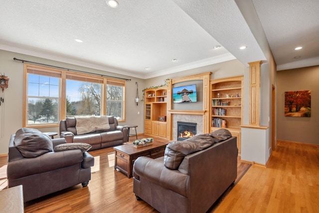 living room with light wood finished floors, ornate columns, a textured ceiling, a tiled fireplace, and crown molding