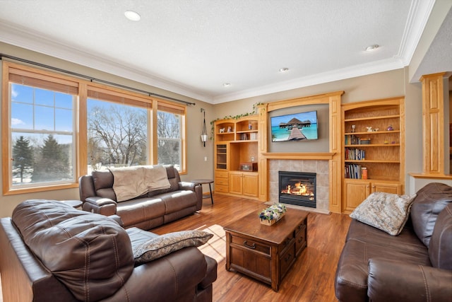 living room featuring a textured ceiling, wood finished floors, crown molding, and a tile fireplace