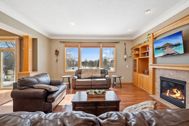 living area with a textured ceiling, crown molding, wood finished floors, and a tile fireplace