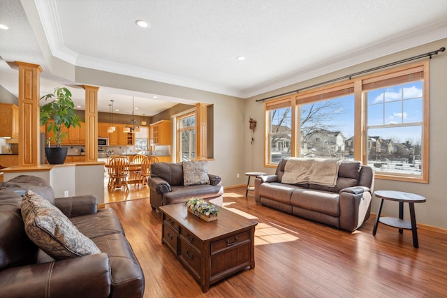 living area with a textured ceiling, hardwood / wood-style flooring, crown molding, and ornate columns