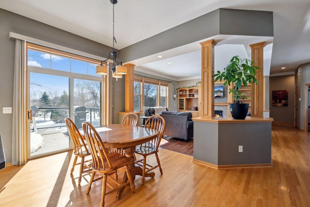 dining area featuring recessed lighting, light wood finished floors, a warm lit fireplace, and ornate columns