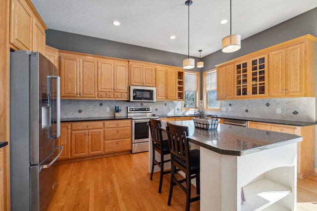 kitchen with light wood-type flooring, open shelves, a center island, appliances with stainless steel finishes, and a breakfast bar area