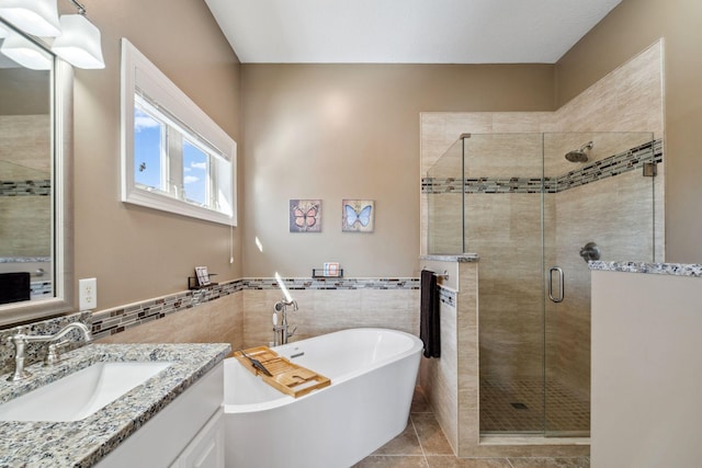 full bath with tile patterned flooring, vanity, a stall shower, a freestanding tub, and tile walls