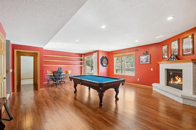 recreation room featuring a brick fireplace, a textured ceiling, baseboards, and wood finished floors