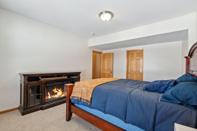 bedroom with baseboards, light colored carpet, and a glass covered fireplace