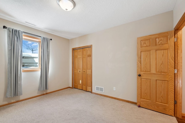 unfurnished bedroom featuring visible vents, light carpet, a textured ceiling, and baseboards