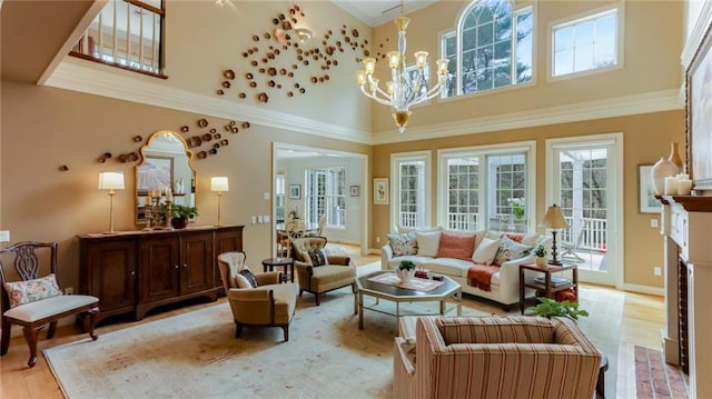 living area featuring a fireplace, a towering ceiling, light wood-style flooring, ornamental molding, and a chandelier