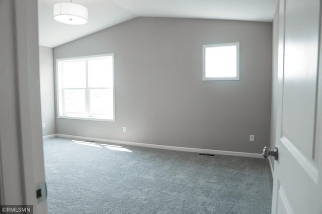 empty room featuring visible vents, a healthy amount of sunlight, lofted ceiling, and carpet