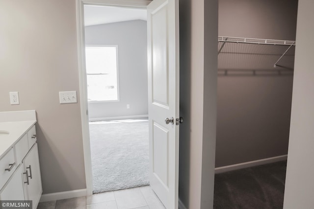 bathroom with a walk in closet, tile patterned floors, vanity, and baseboards