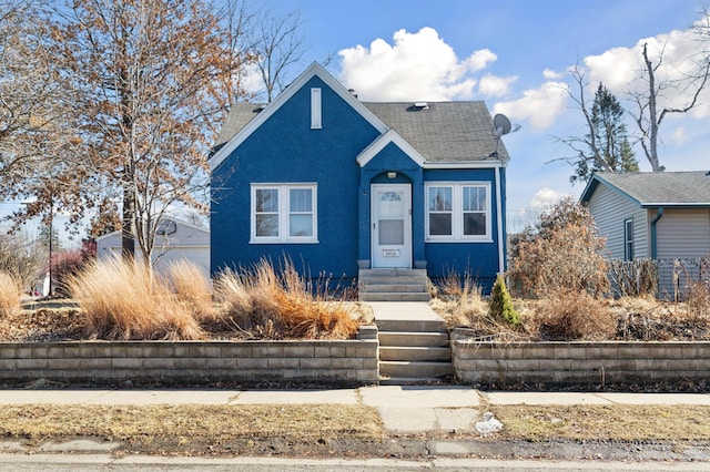 bungalow-style home with entry steps, a shingled roof, and stucco siding