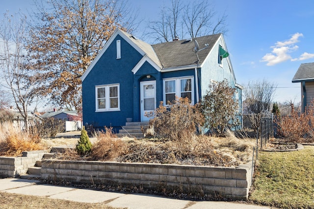 bungalow-style home featuring a shingled roof, fence, and stucco siding