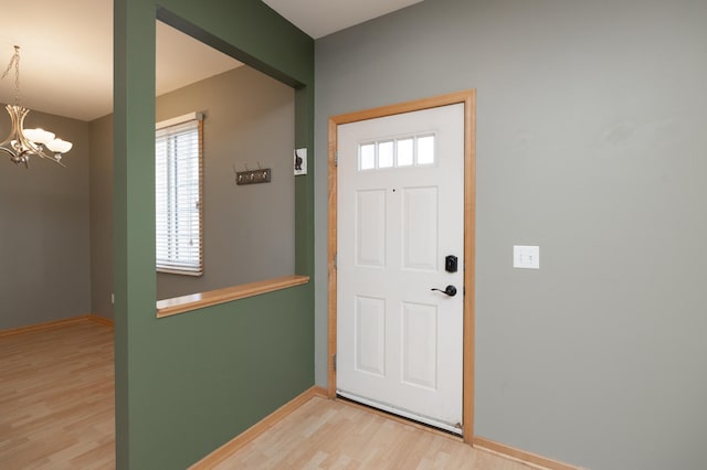 foyer entrance with baseboards, light wood-style flooring, and an inviting chandelier