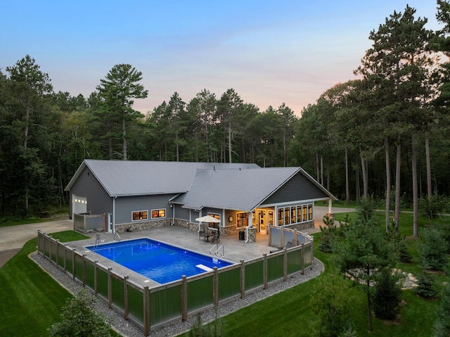 back of house with metal roof, stone siding, a lawn, and a view of trees