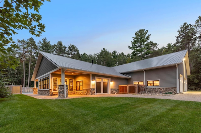 rear view of property with driveway, a lawn, stone siding, metal roof, and fence