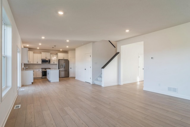 unfurnished living room featuring stairs, light wood-style flooring, visible vents, and recessed lighting