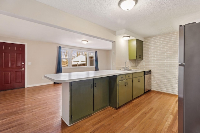 kitchen featuring light wood finished floors, stainless steel appliances, light countertops, a sink, and a peninsula