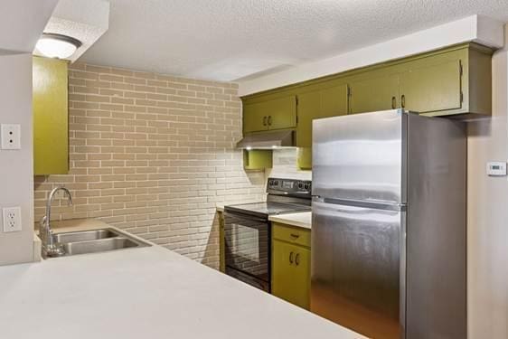 kitchen with under cabinet range hood, a sink, black electric range, light countertops, and freestanding refrigerator