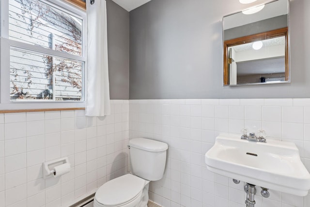 half bathroom featuring toilet, a wainscoted wall, tile walls, and a sink