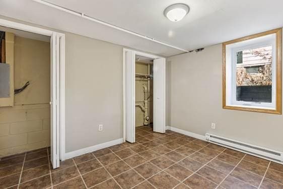 unfurnished bedroom with a baseboard heating unit, dark tile patterned floors, a closet, and baseboards