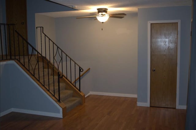 stairs with a ceiling fan, a textured ceiling, baseboards, and wood finished floors