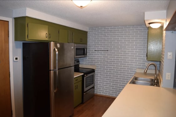 kitchen with light countertops, green cabinets, appliances with stainless steel finishes, a sink, and brick wall