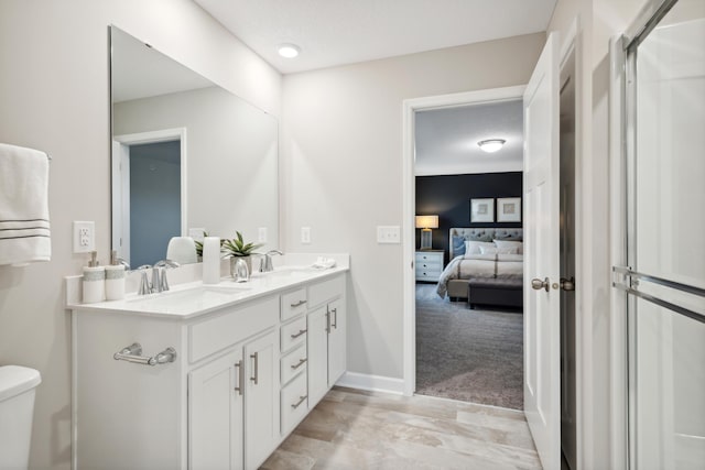 ensuite bathroom featuring toilet, a sink, baseboards, double vanity, and ensuite bath