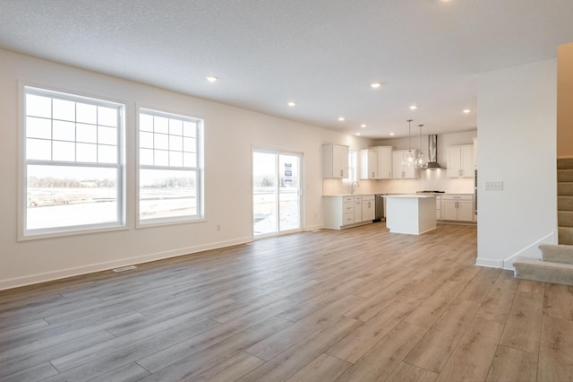 unfurnished living room featuring light wood-style floors, stairs, baseboards, and a sink