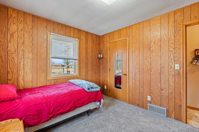 bedroom with carpet, visible vents, wood walls, and a textured ceiling