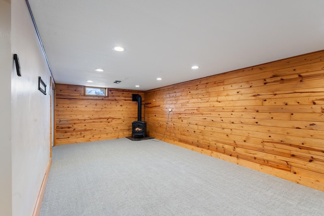 basement featuring wood walls, carpet, a wood stove, and recessed lighting