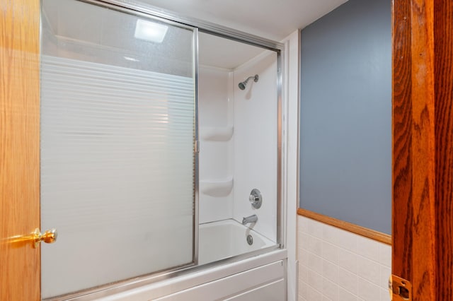 bathroom featuring a wainscoted wall, bath / shower combo with glass door, and tile walls