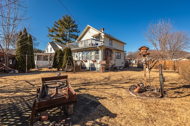 back of property with a balcony, a chimney, and fence