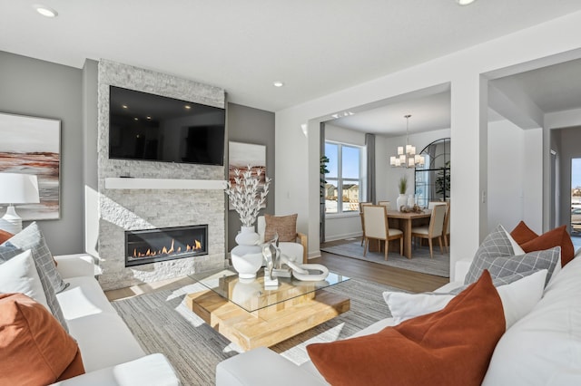 living room with baseboards, wood finished floors, a stone fireplace, a chandelier, and recessed lighting