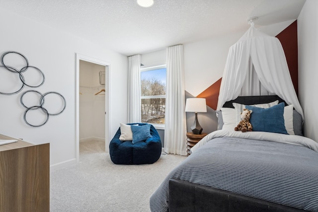 bedroom with a textured ceiling, baseboards, a walk in closet, and carpet flooring