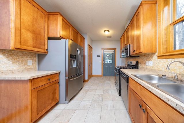 kitchen with a sink, light countertops, appliances with stainless steel finishes, tasteful backsplash, and brown cabinetry