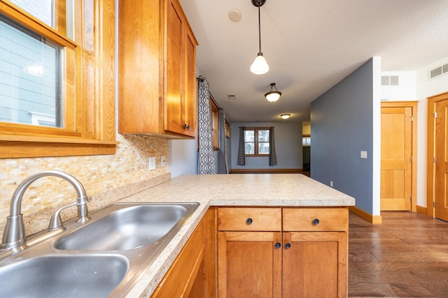 kitchen featuring a peninsula, a sink, backsplash, brown cabinetry, and decorative light fixtures