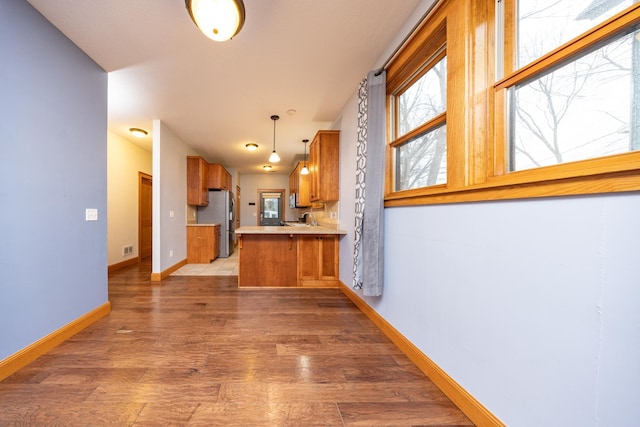 kitchen featuring baseboards, brown cabinetry, light wood-style flooring, freestanding refrigerator, and a peninsula