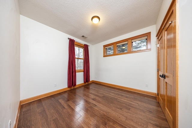 spare room featuring dark wood-style floors, baseboards, visible vents, and a textured ceiling