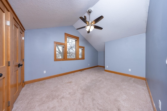 additional living space with baseboards, light colored carpet, lofted ceiling, ceiling fan, and a textured ceiling