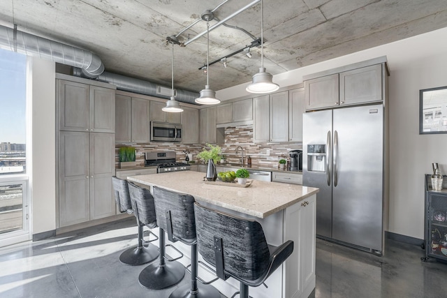 kitchen featuring appliances with stainless steel finishes, decorative light fixtures, a center island, concrete flooring, and backsplash