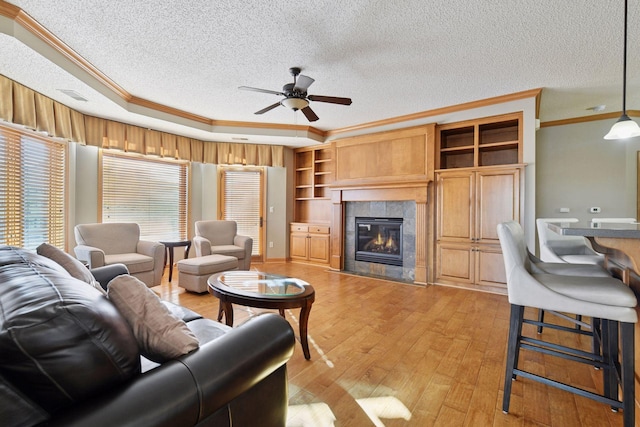 living room with a tray ceiling, a tile fireplace, light wood-style floors, a textured ceiling, and crown molding