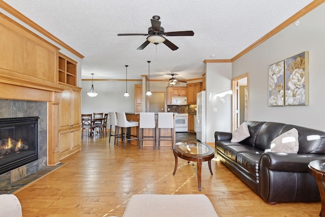 living room featuring a tile fireplace, a textured ceiling, light wood-type flooring, and crown molding