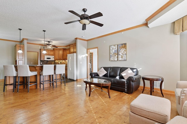 living area with crown molding, baseboards, light wood-type flooring, and a textured ceiling