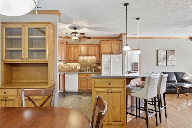 kitchen featuring a sink, backsplash, a kitchen island, white appliances, and a breakfast bar area